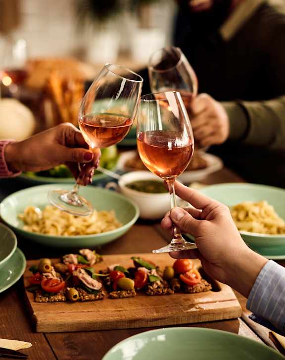A group of people toasting with wine glasses in front of a meal.