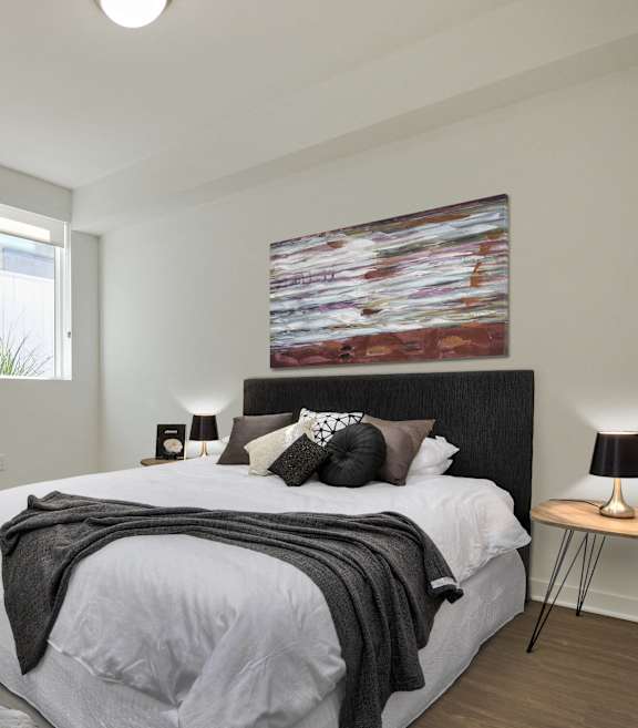 A bedroom with a large bed, a blue chair, and a painting on the wall.