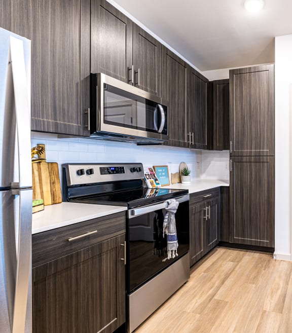 a kitchen with dark wood cabinets and stainless steel appliances and a sink at The Parker Austin, Pflugerville, 78660