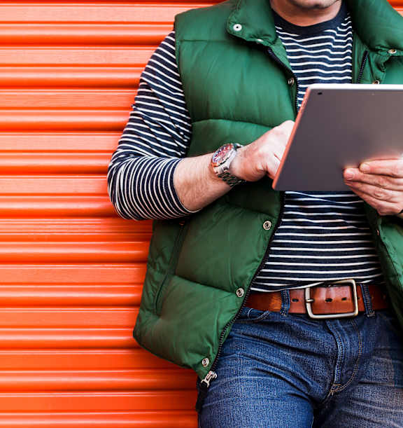 A person in a green vest and striped shirt is holding a tablet.