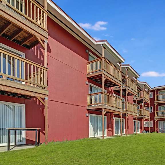 A row of red apartments with balconies and a green lawn at Bay Arms Apartments. 