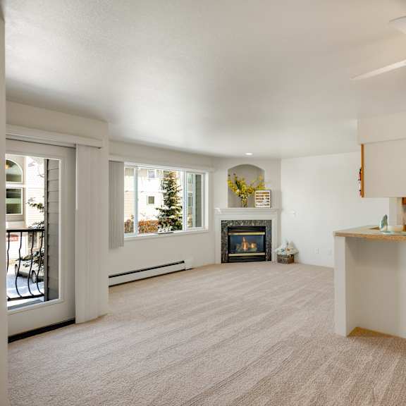 An empty living room with hardwood flooring and kitchen with a door to a balcony at La Maisonette Apartments. 