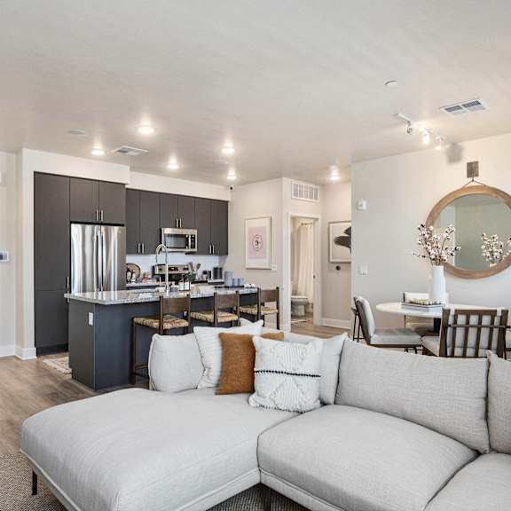 A living room with a couch, and behind it, a kitchen and dining room with a dining table and chairs, and a refrigerator, counters, barstool chairs, a microwave, and an oven at Dobson Ranch.