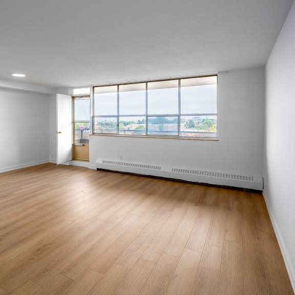A room with wooden flooring and a large window overlooking a body of water.