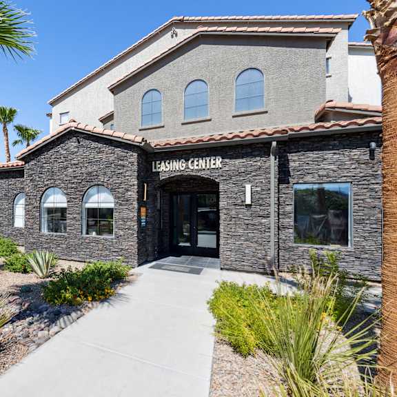 A building with a stone facade and a sign that reads "LEASING CENTER" is surrounded by palm trees and small bushes.
