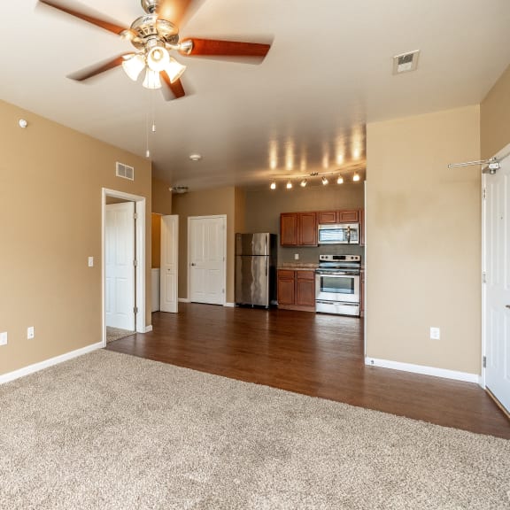 an empty living room with a ceiling fan and a kitchen