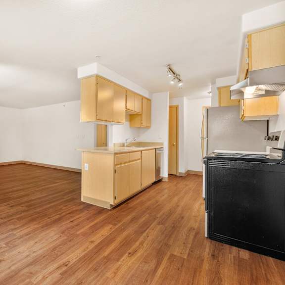 an empty living room and kitchen with wood flooring and a door to the kitchen