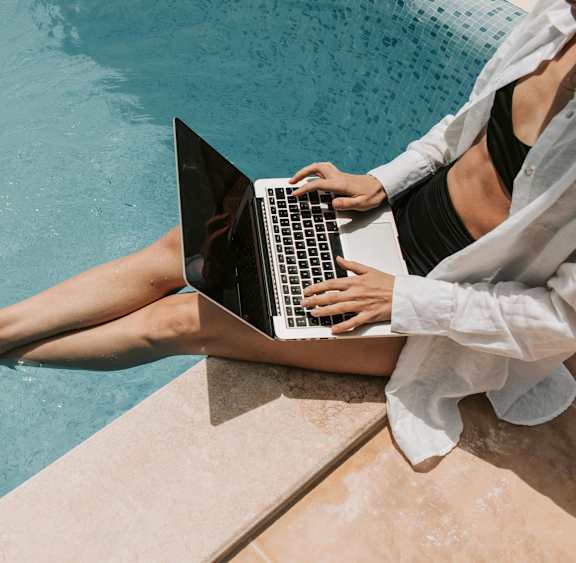 A person is sitting by a pool using a laptop.