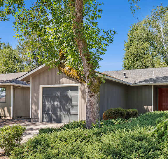 A house with a red door and a garage door is surrounded by greenery.