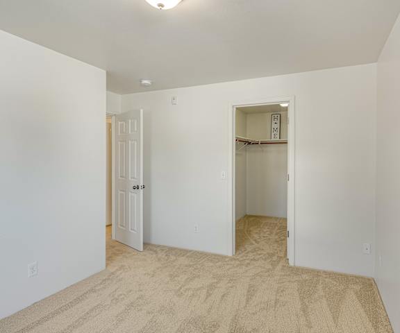 An empty carpeted bedroom with a closet at La Maisonette Apartment Homes. 