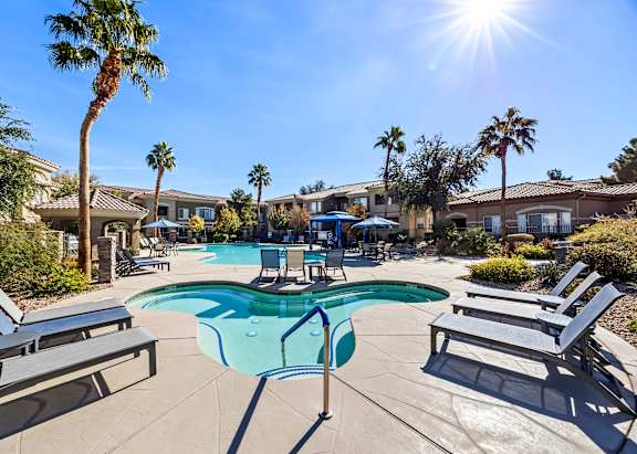 A sunny day at the pool with lounge chairs and palm trees.