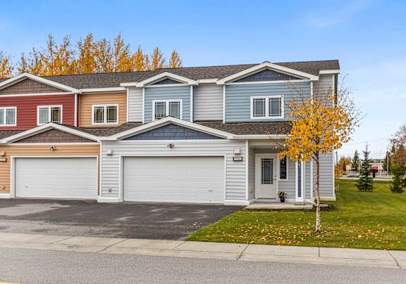 A row of houses with garages and a tree with yellow leaves.