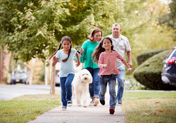 A family of four running on a sidewalk with a dog.
