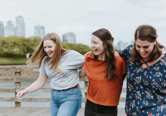 Three women are laughing and having fun on a wooden pier.