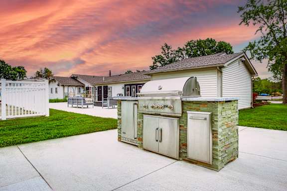 A backyard with a white fence and a stone and wood outdoor kitchen.