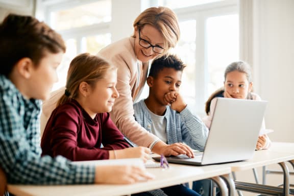 a teacher is teaching a group of students how to use a laptop