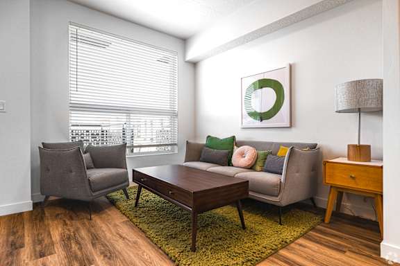 A living room with a grey couch, a brown coffee table, and a green rug.