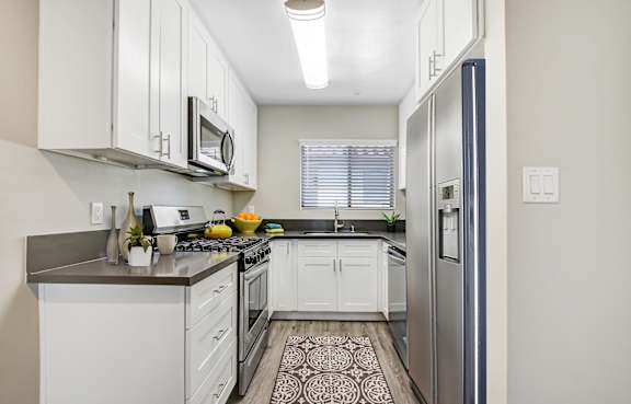 A kitchen with white cabinets and a black and white patterned rug on the floor.