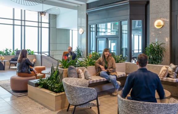 a group of people sitting in a lobby with furniture and plants