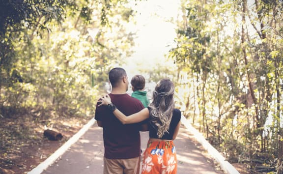 a man and woman holding a child walking down a path