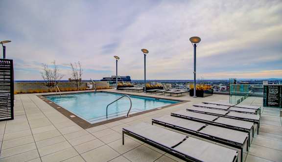 A pool with sun loungers and lights on the side.