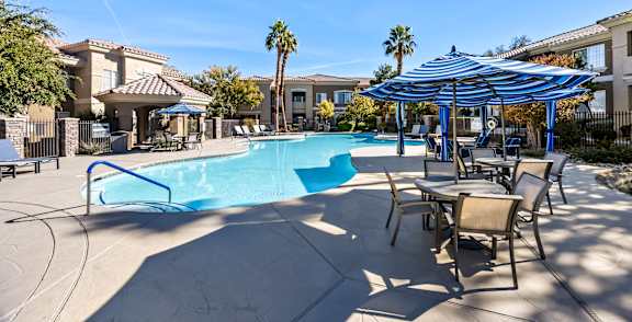 A swimming pool with a blue umbrella and chairs around it.