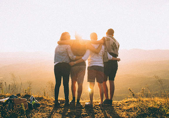Four friends are standing together and enjoying the sunset.