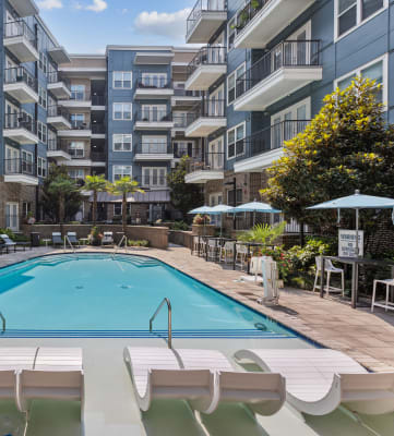 an outdoor swimming pool with lounge chairs and umbrellas in front of an apartment building