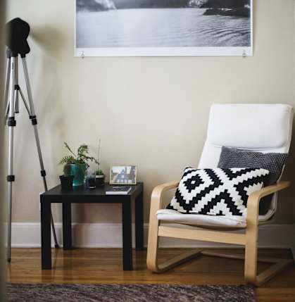 a white chair with a black and white pillow next to a table with a tripod