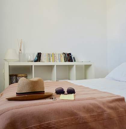 a bed with a white bedspread and a hat and sunglasses on it