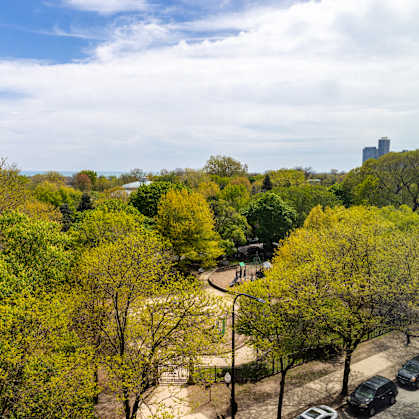 A park with trees and a playground in the foreground and a city skyline in the background.at The Nest at Lincoln Park West, Chicago, IL