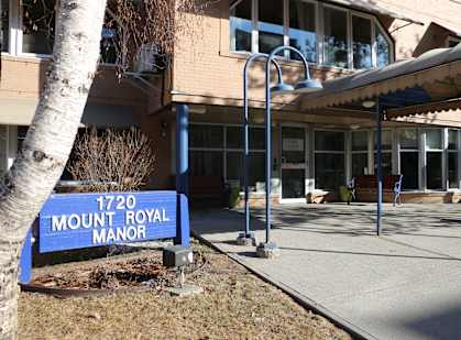 A blue sign that says Mount Royal Manor stands in front of a building.
