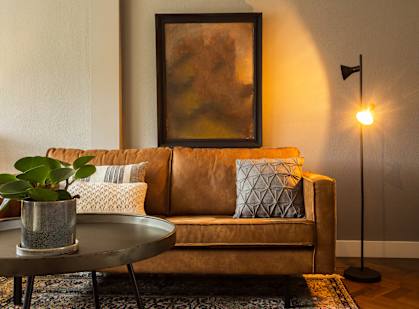 a living room with a brown couch and a painting on the wall