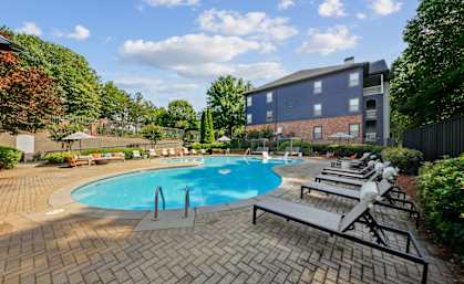A swimming pool surrounded by a brick patio and lounge chairs.