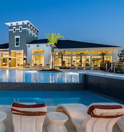 A poolside lounge area with white chairs and a building in the background.