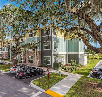 an apartment building with a parking lot and trees in front of it