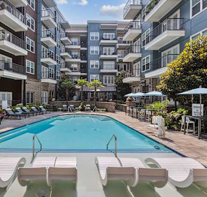 an outdoor swimming pool with lounge chairs and umbrellas in front of an apartment building
