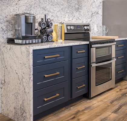 A kitchen with dark blue drawers and a marble countertop.