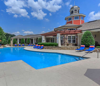 a large swimming pool with lounge chairs and umbrellas in front of a house