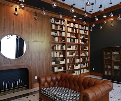 A brown leather couch sits in front of a bookshelf in a room with wooden walls.