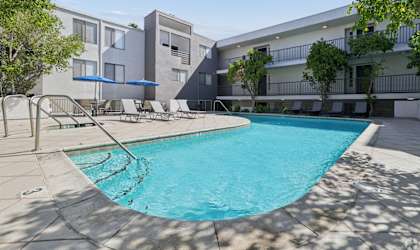 A swimming pool in front of a building with a blue umbrella.
