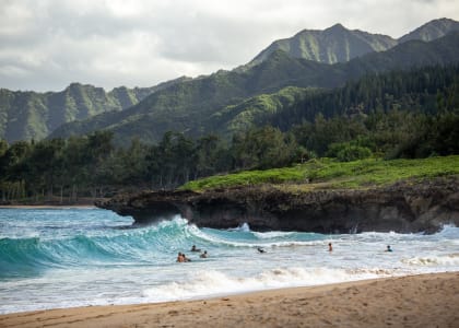 people swimming in the ocean at a beach with mountains in the background Mala Grove in Waipahu, HI
