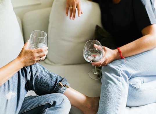 Two people sitting on a couch holding wine glasses.