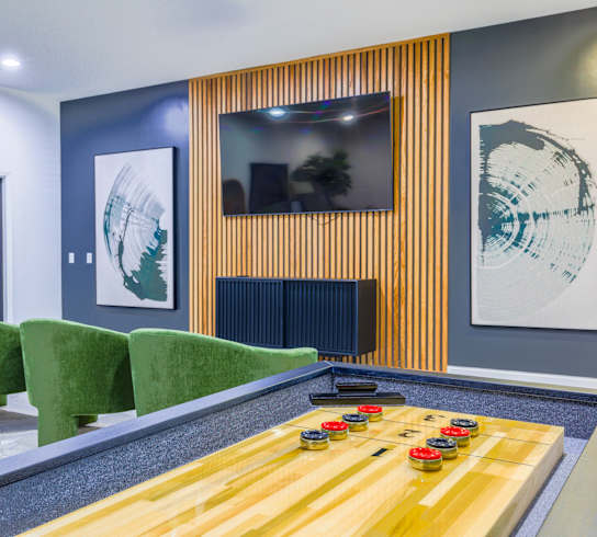 A game room with a shuffleboard table and green chairs.