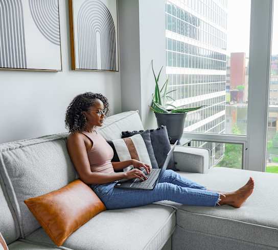 A woman is sitting on a couch using a laptop. at The Washington at Chatham, Pittsburgh Pennsylvania