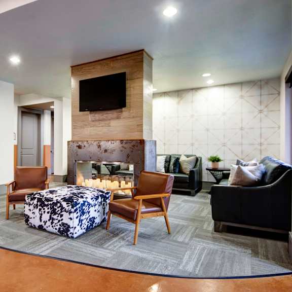 The resident lounge at Sorrel Fairview Apartment Homes with black leather couches, brown leather and wood chairs, a fireplace with candles lighting it, and a TV. 