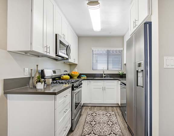 A kitchen with white cabinets and a black and white patterned rug on the floor.