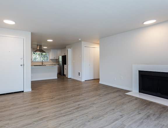 A white interior with a fireplace and a kitchen in the background at Ellyson Apartment Homes in Tacoma, WA