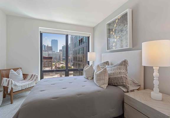A bedroom with a large bed, a chair, and a view of the city.