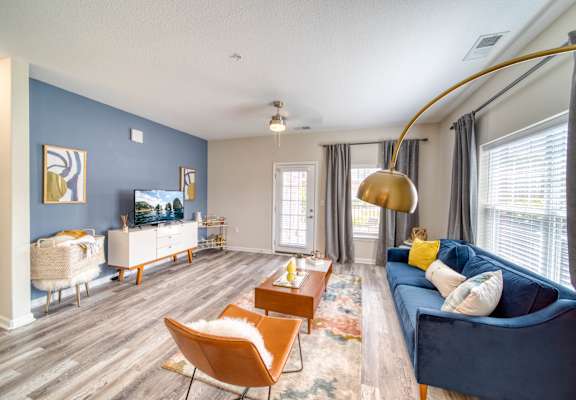 a living room with a blue couch and chairs and a flat screen tv on the wall at Meridian Obici, Suffolk, 23434